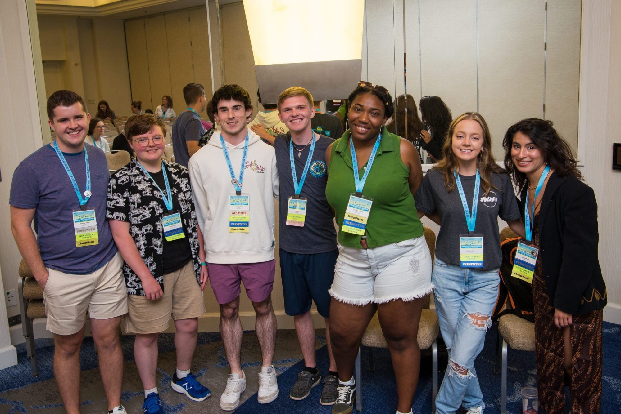 Group of eight diverse teens smiling and posing together at a conference, wearing name badges and casual attire.