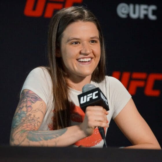 A female ufc fighter with a visible arm tattoo smiles while speaking into a ufc microphone during the 41st Annual NSA Conference.