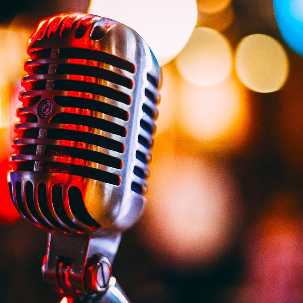 Vintage-style microphone in sharp focus against a blurred background of warm, colorful bokeh lights during a music tour.