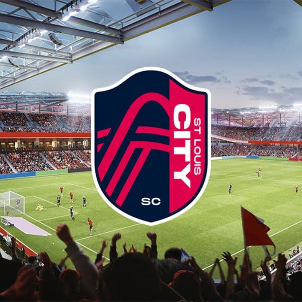 An energetic soccer match scene in a stadium filled with fans. In the foreground is the logo of St. Louis City SC, featuring pink and navy colors, becoming a popular stop on local sports tours.