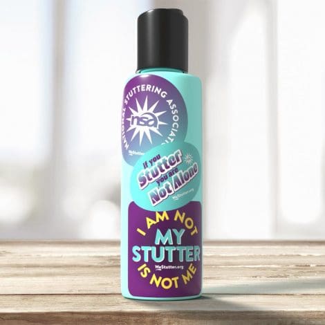 A vibrant turquoise lotion bottle labeled "WE Stutter Stickers" with slogans "i stutter. so what?" and "i am not my stutter" placed on a wooden surface near a sunlit window.